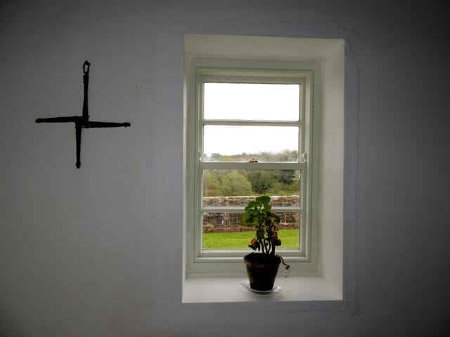 A St Brigid's Cross hanging on a white wall in an Irish home with a small window next to it. 