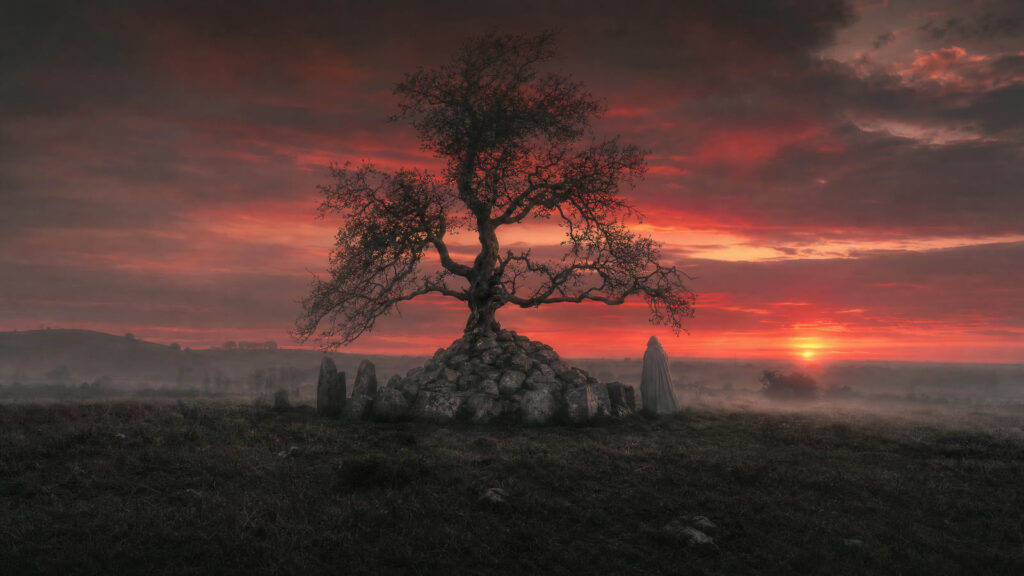 An ancient stone cairn under a hawthorn tree at dusk in County Derry with a faint cloaked figure beside it