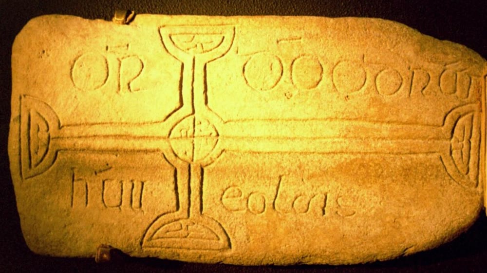 Stone grave slab carved with a long cross with rounded ends, with the words OR DO and a name in early medieval Irish lettering around its arms
