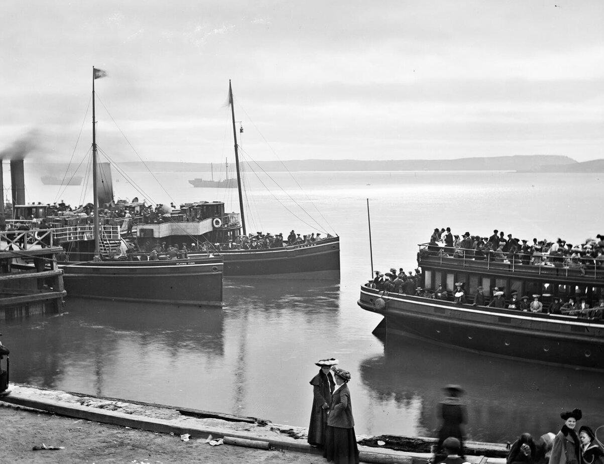 Old photograph of emigrants crowding steam tenders at Scott's Quay, Queenstown (Cobh), waiting to be taken out to a transatlantic liner. Crop the handwritten catalogue text at the edges