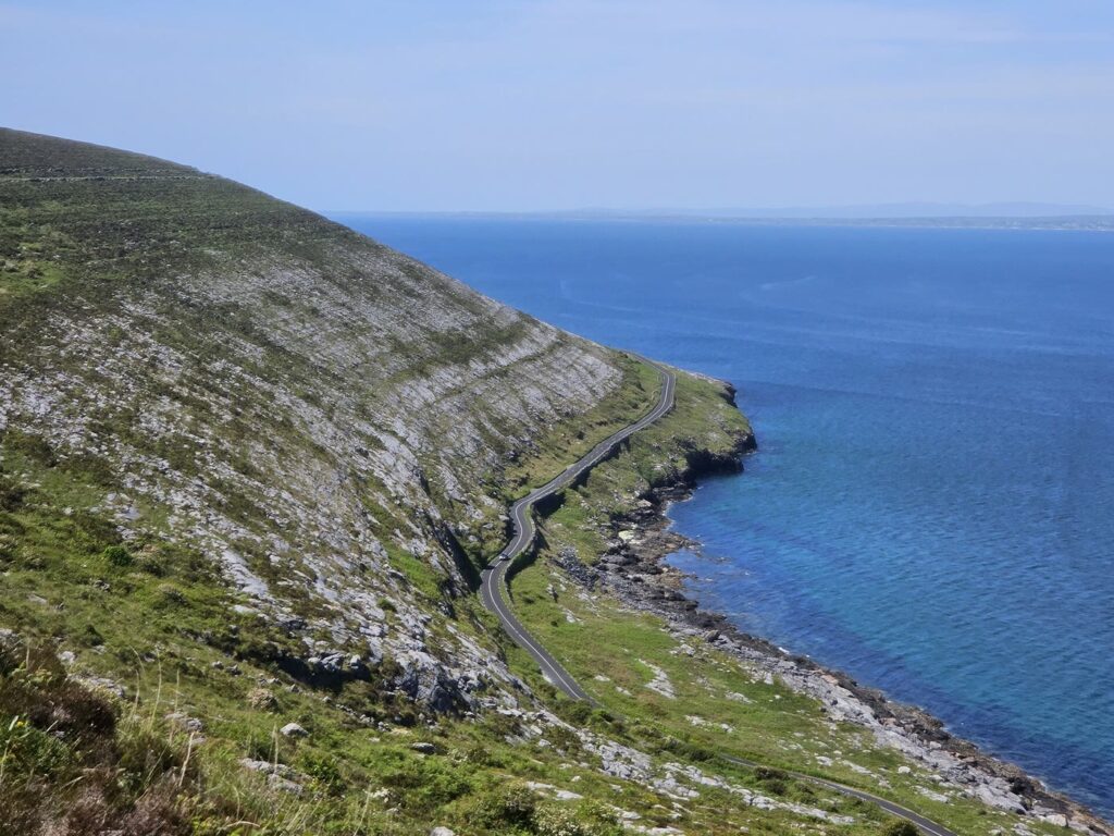 Grey limestone hills of the Burren sloping down to a winding coast road and the blue sea near Fanore, Co. Clare
