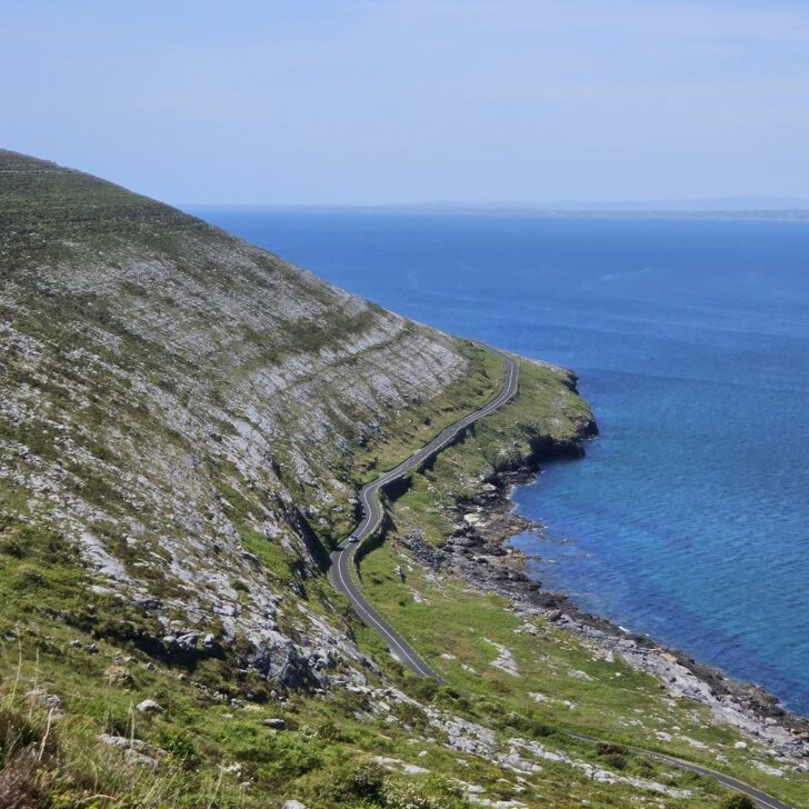 Grey limestone hills of the Burren sloping down to a winding coast road and the blue sea near Fanore, Co. Clare