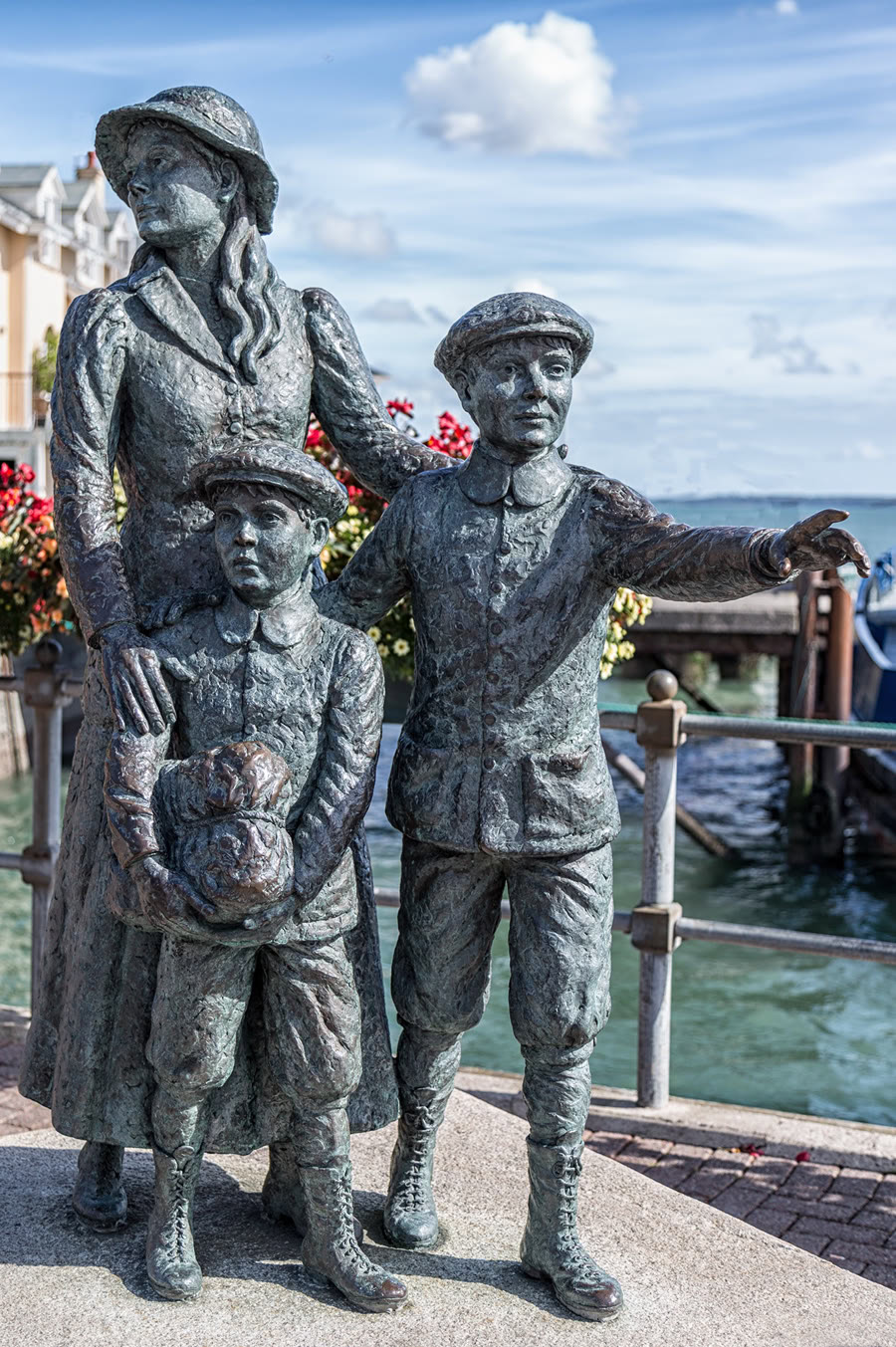 Bronze statue at Cobh of Annie Moore with her hand on her younger brother's shoulder while her other brother points out to sea, with Cork Harbour behind