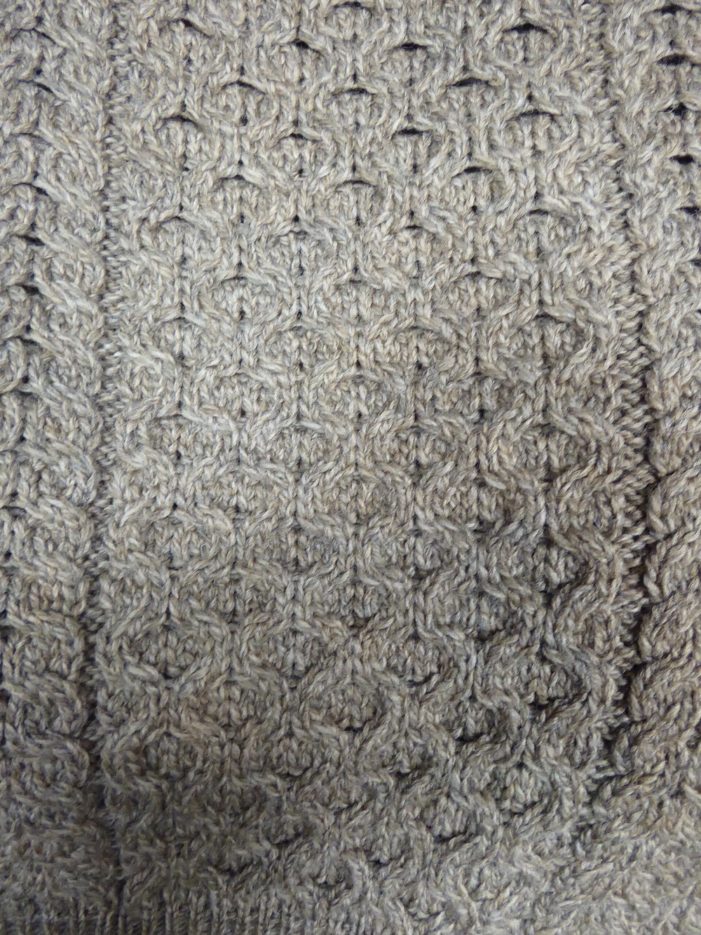 Close-up of oatmeal-coloured Aran knitting with a central honeycomb panel framed by twisted cables