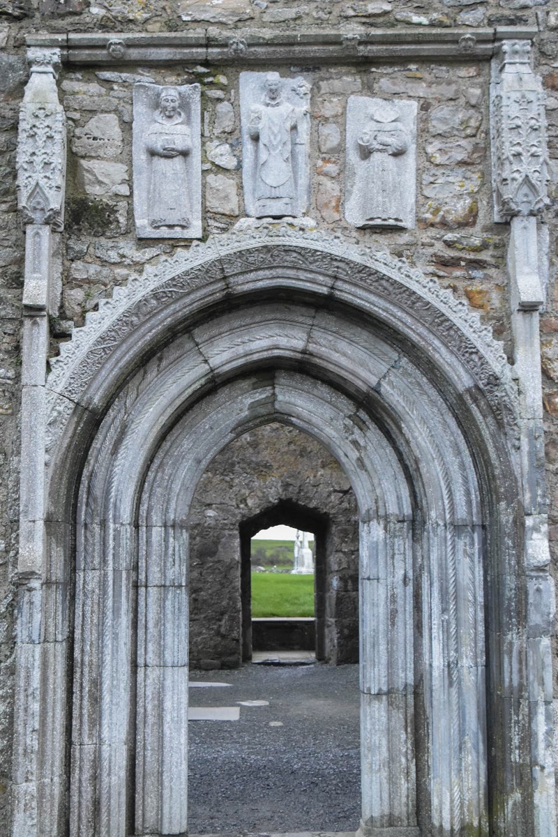Clonmacnoise Whispering Arch: a pointed Gothic doorway with deeply carved mouldings, under three carved stone figures of saints set into the cathedral wall