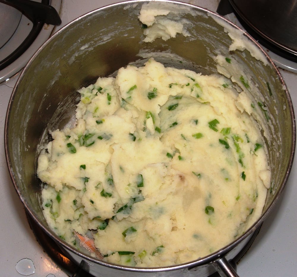 A saucepan of champ on a stove: creamy mashed potato flecked with chopped green scallions