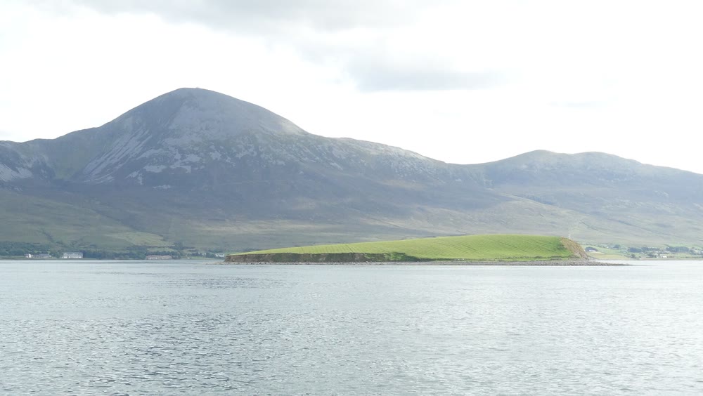 Long low green island in the grey water of Clew Bay, with the slopes and rounded summit of Croagh Patrick rising behind it