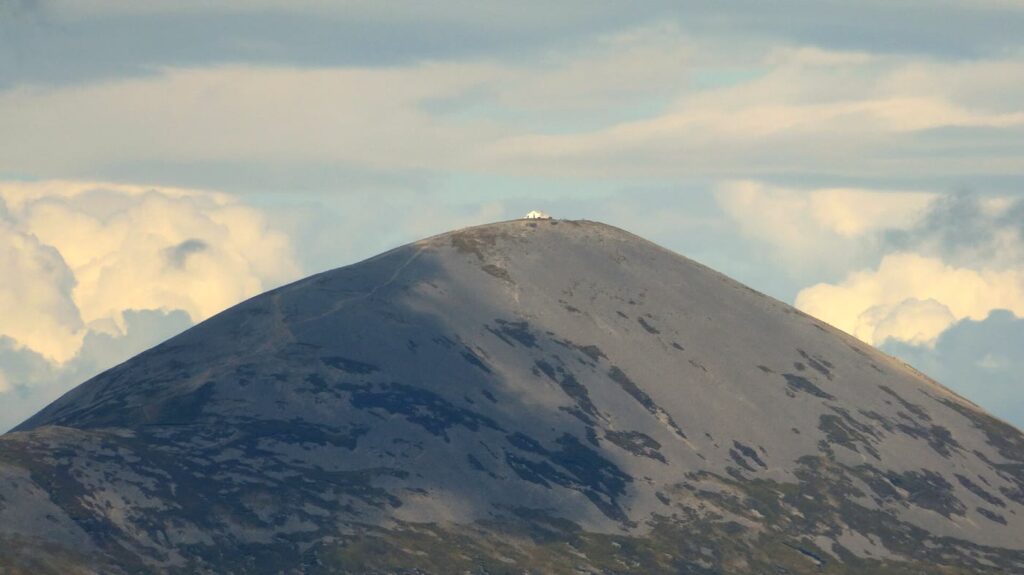 Croagh Patrick: the grey cone of Ireland's holy mountain with the small white summit chapel on top, against a cloudy sky