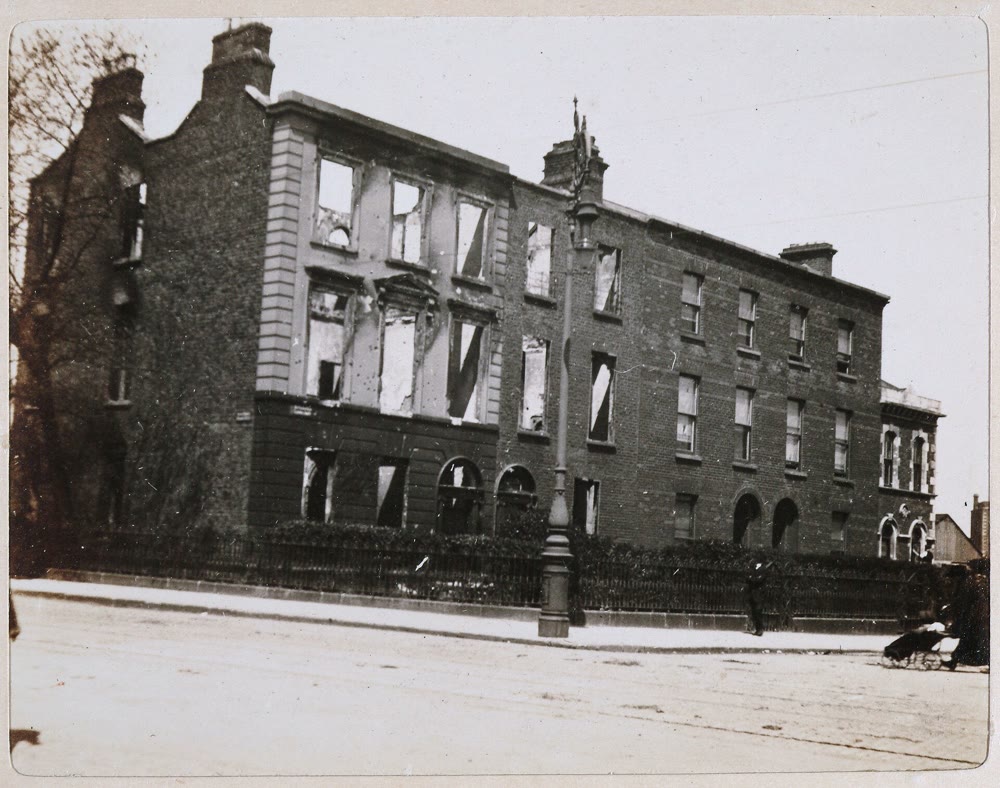 A burned-out corner house with empty windows beside a terrace of brick houses at Clanwilliam Place in Dublin, by Mount Street Bridge, in May 1916