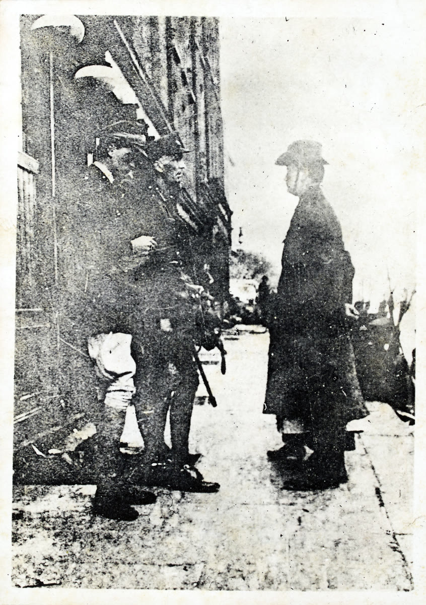 Patrick Pearse in a long coat and hat faces two British officers on a Dublin street in 1916, with a figure almost hidden behind him