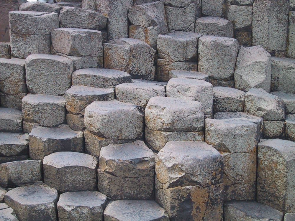 Close-up of grey basalt columns at the Giant's Causeway, packed together at different heights, with five and six-sided tops, some slightly hollowed