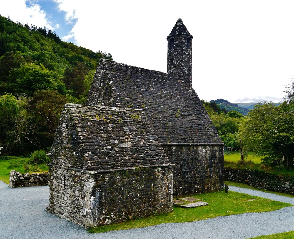 St Kevin's Kitchen at Glendalough: a small stone church with a steep stone roof and a slender round belfry, surrounded by gravel paths and wooded hills