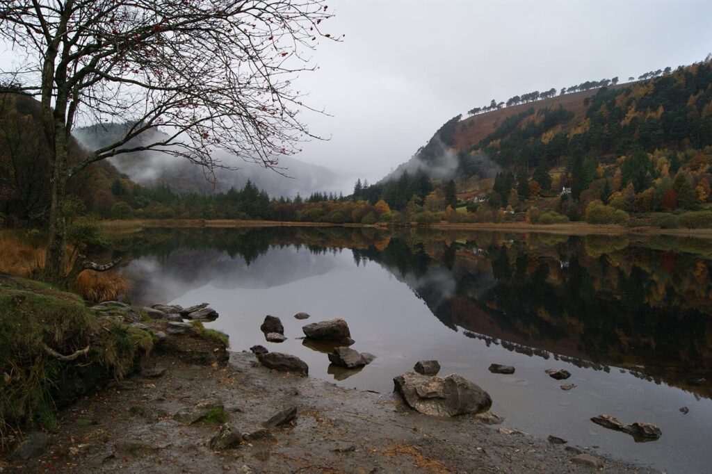 The Upper Lake at Glendalough in autumn, with still water reflecting the wooded valley sides and low mist on the hills