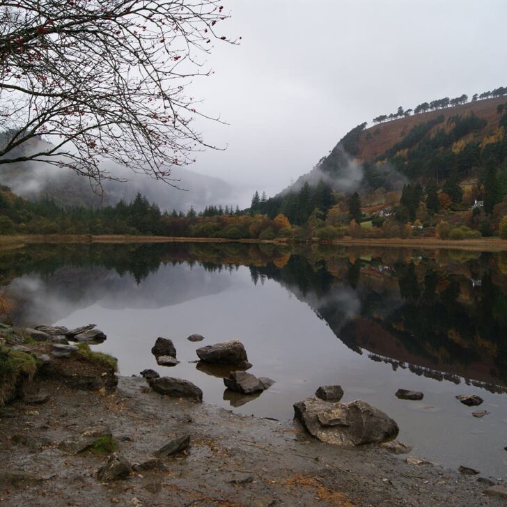 The Upper Lake at Glendalough in autumn, with still water reflecting the wooded valley sides and low mist on the hills