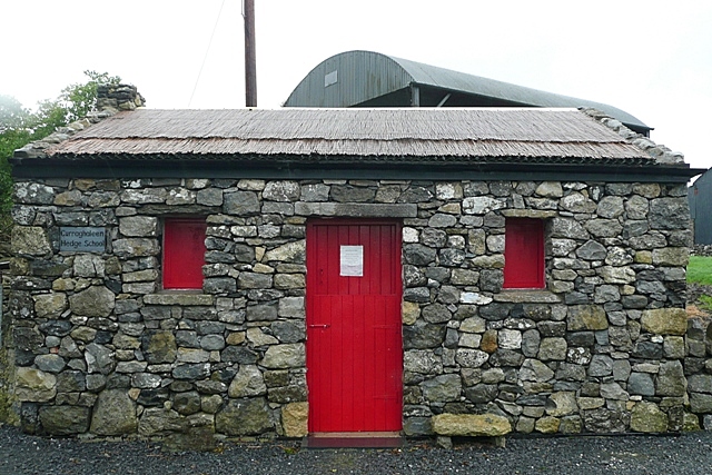 A restored stone barn with a thatched roof, a red door and a small plaque reading Curraghaleen Hedge School, in Co. Roscommon