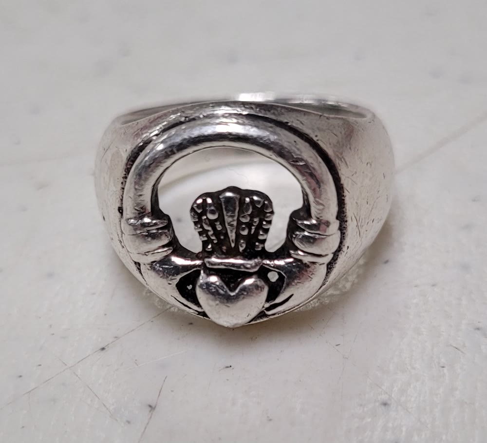 A worn sterling silver Claddagh ring showing two hands holding a crowned heart, on a pale surface