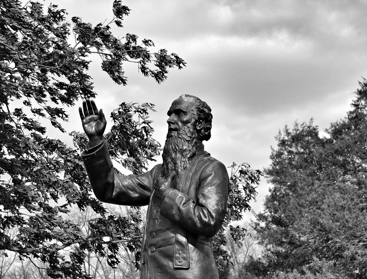 Bronze statue of Father William Corby at Gettysburg, a bearded priest raising his right hand in blessing, framed by trees and a cloudy sky