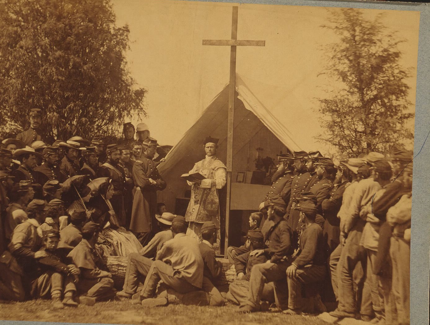 1861 photograph of soldiers of the 69th New York gathered around a priest at an outdoor altar under a tall wooden cross, with a tent behind
