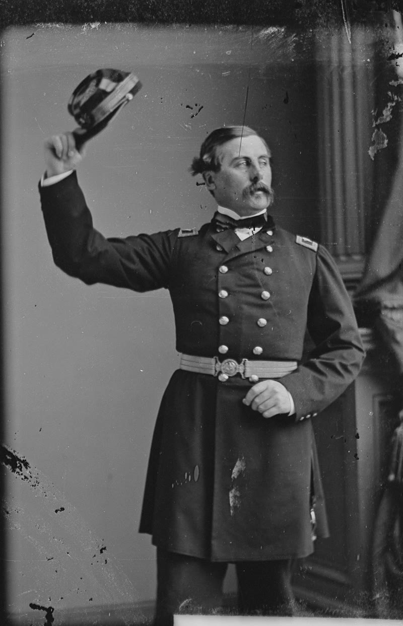 Black and white studio photograph of Thomas Francis Meagher in a Union officer's frock coat, raising his hat in his right hand