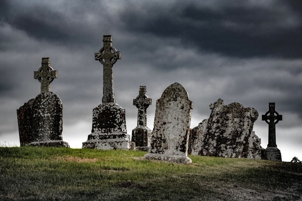 Weathered Celtic cross headstones and old gravestones on a grassy rise at Clonmacnoise, Co. Offaly, under a dark, cloudy sky