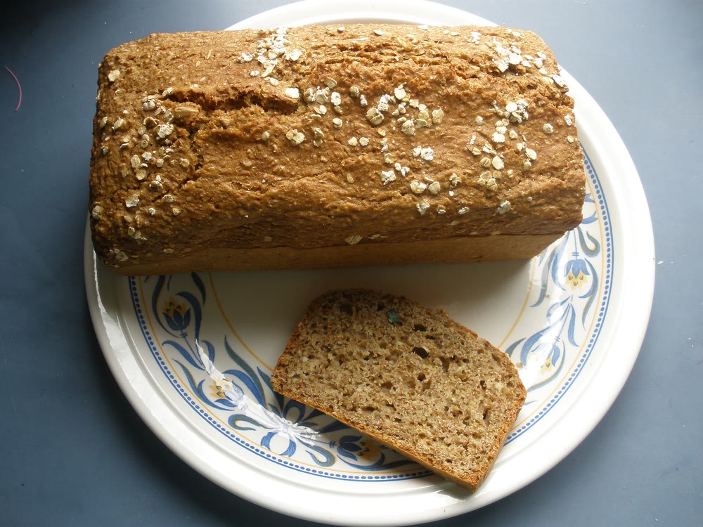 A tin loaf of brown soda bread topped with oat flakes on a white plate with a blue flower pattern, with one thick slice cut