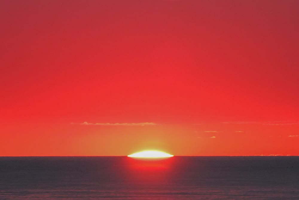 The sun rising over a calm Irish Sea under a deep red sky, seen from the beach at Bray in County Wicklow
