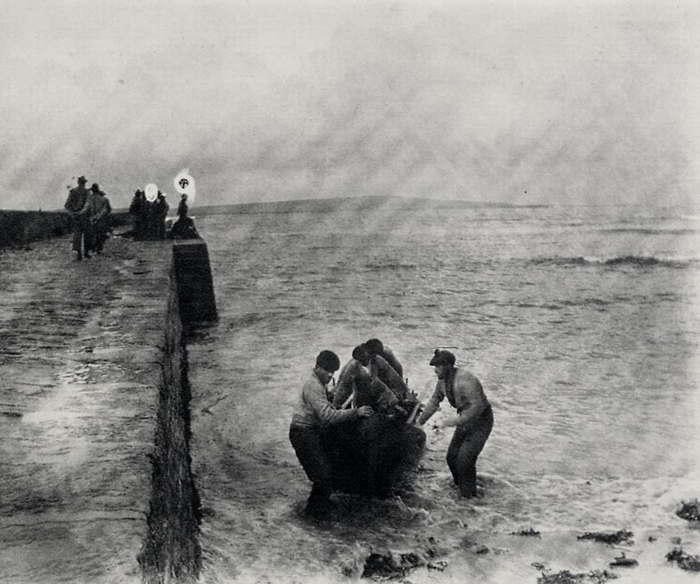 Black and white 1898 photograph of four men hauling a currach out of rough water beside a stone pier on the Aran Islands