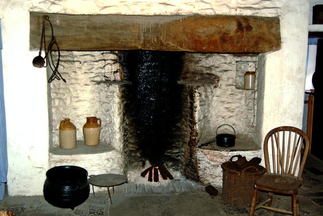 The open hearth of a whitewashed cottage at Bunratty Folk Park, Co. Clare, with a large black cast-iron pot, a small lidded pot and a low iron stand beside the fire