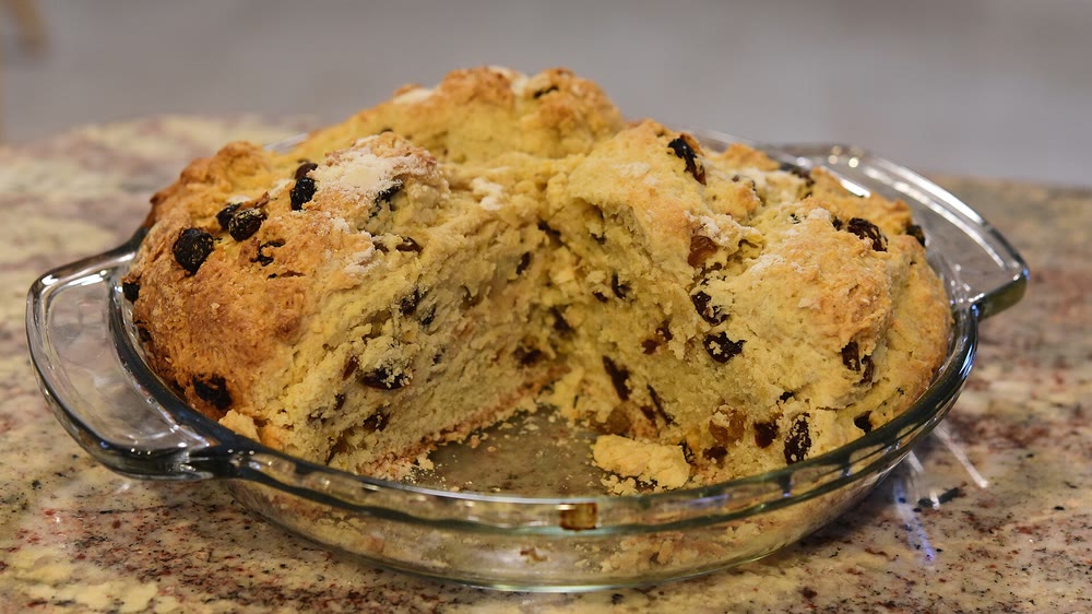 A golden raisin-filled soda bread broken open in a glass pie dish on a granite counter