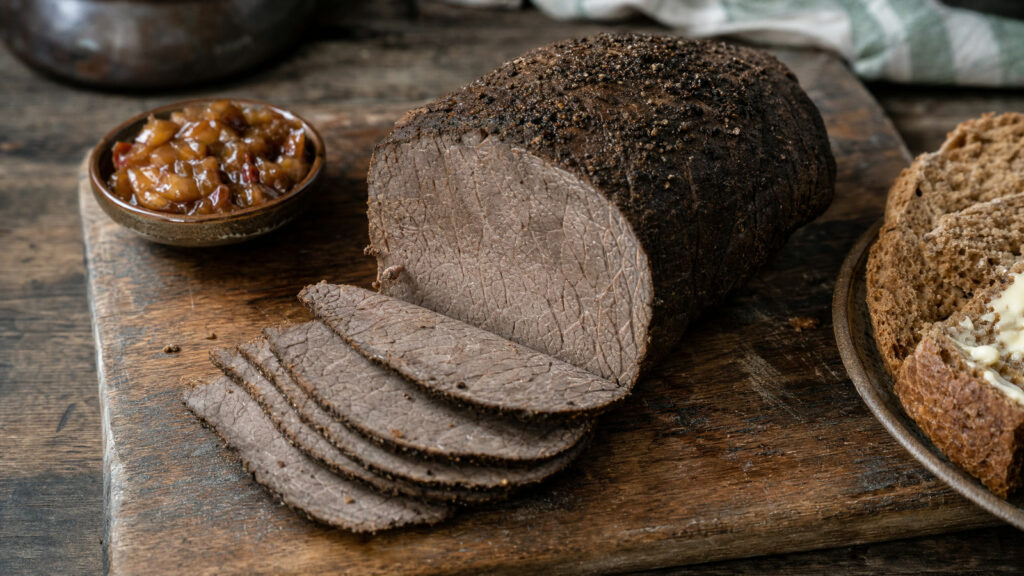 Irish spiced beef on a wooden board with thin grey-brown slices, brown bread and chutney
