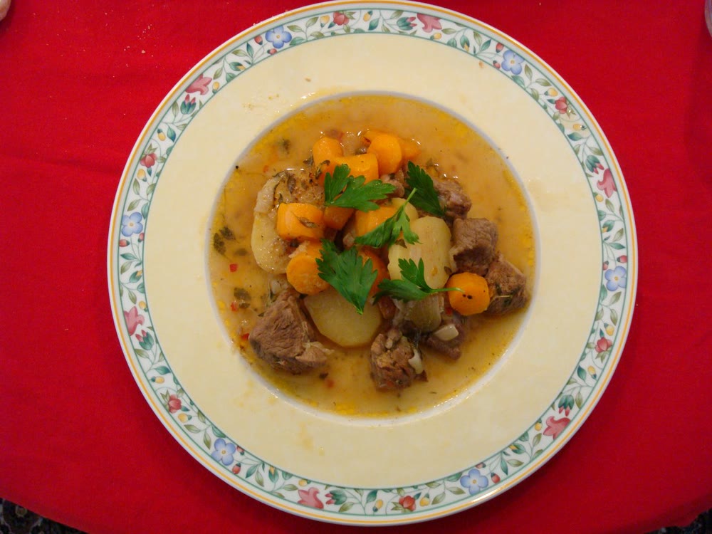 A plate of Irish stew in a pale golden broth: chunks of lamb, potato and carrot topped with sprigs of flat-leaf parsley, on a flowered china plate