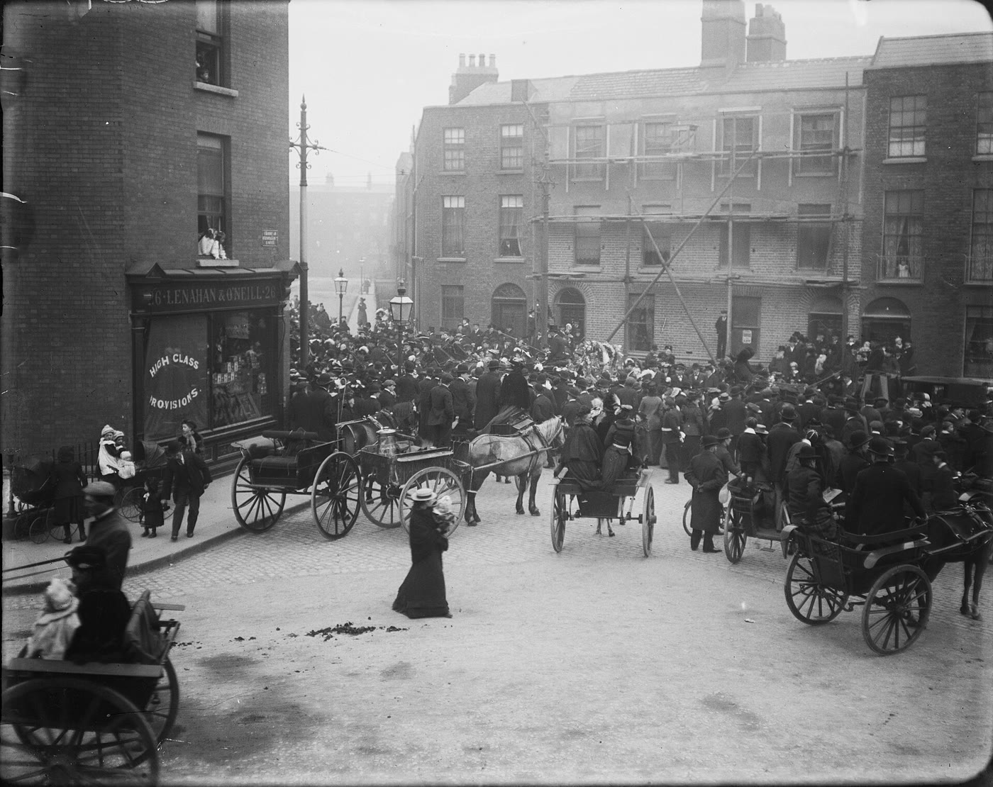 Old black and white photo of a large crowd, with horse-drawn traps and carts, gathered for a funeral on a Dublin street around 1900