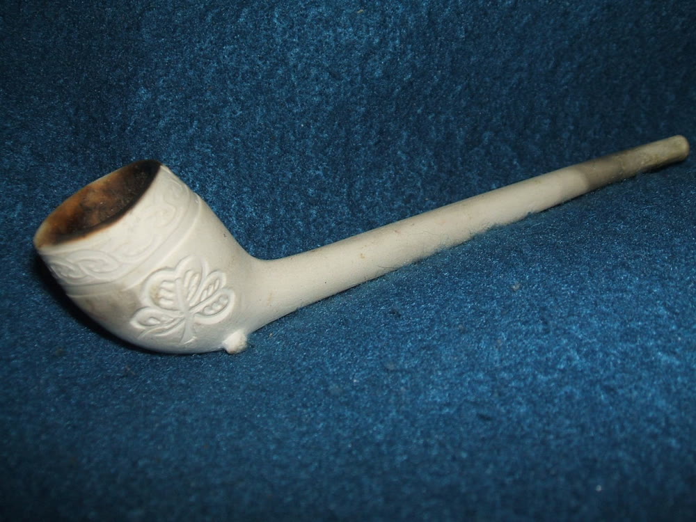 White Irish clay pipe with a short stem and a shamrock moulded on the bowl, lying on blue cloth