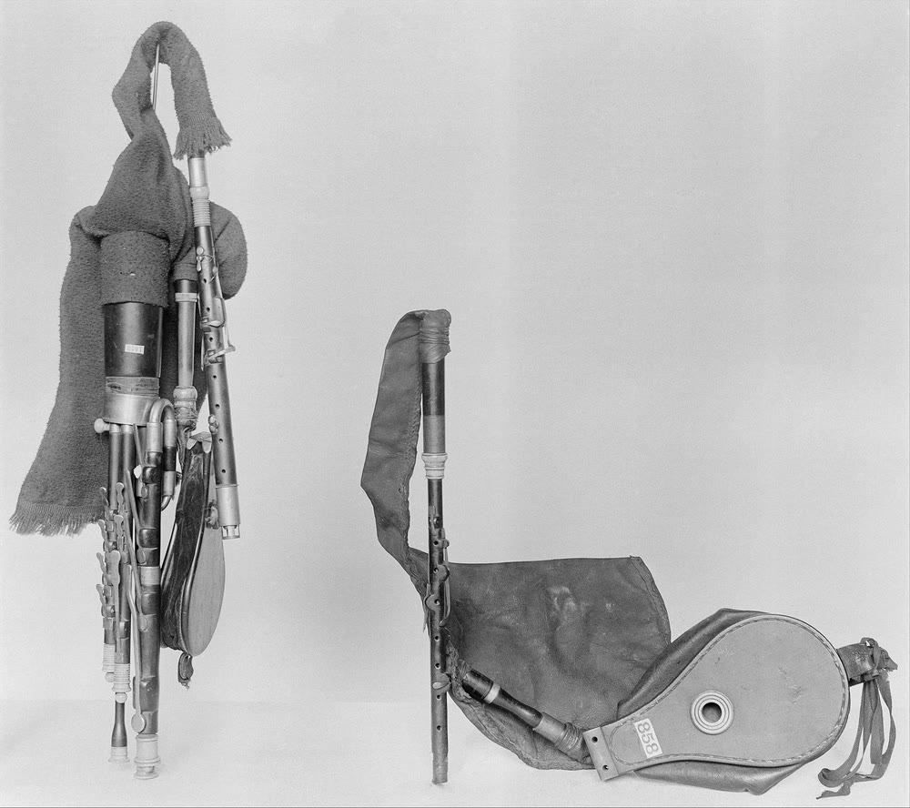 Black-and-white museum photograph of an 18th-century set of Irish uilleann pipes in two parts: the drones and regulators wrapped in cloth, and the chanter, leather bag and elbow bellows