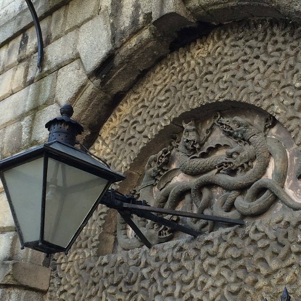 Stone relief of coiled serpents with dragon-like heads in a round panel above the door of Kilmainham Gaol, with an old iron lamp in front