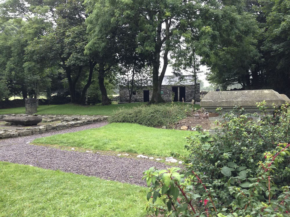 The Michael Collins birthplace at Woodfield in West Cork: a low stone farm building among trees, with lawns, a gravel path and low stone foundations in the foreground