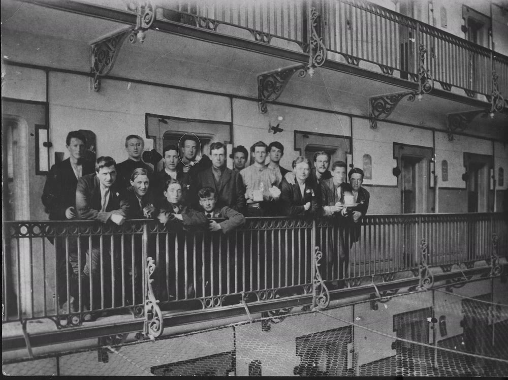 A group of young Irish prisoners in jackets lean on an iron railing on a landing inside Stafford Gaol in 1916, with Michael Collins circled in the back row