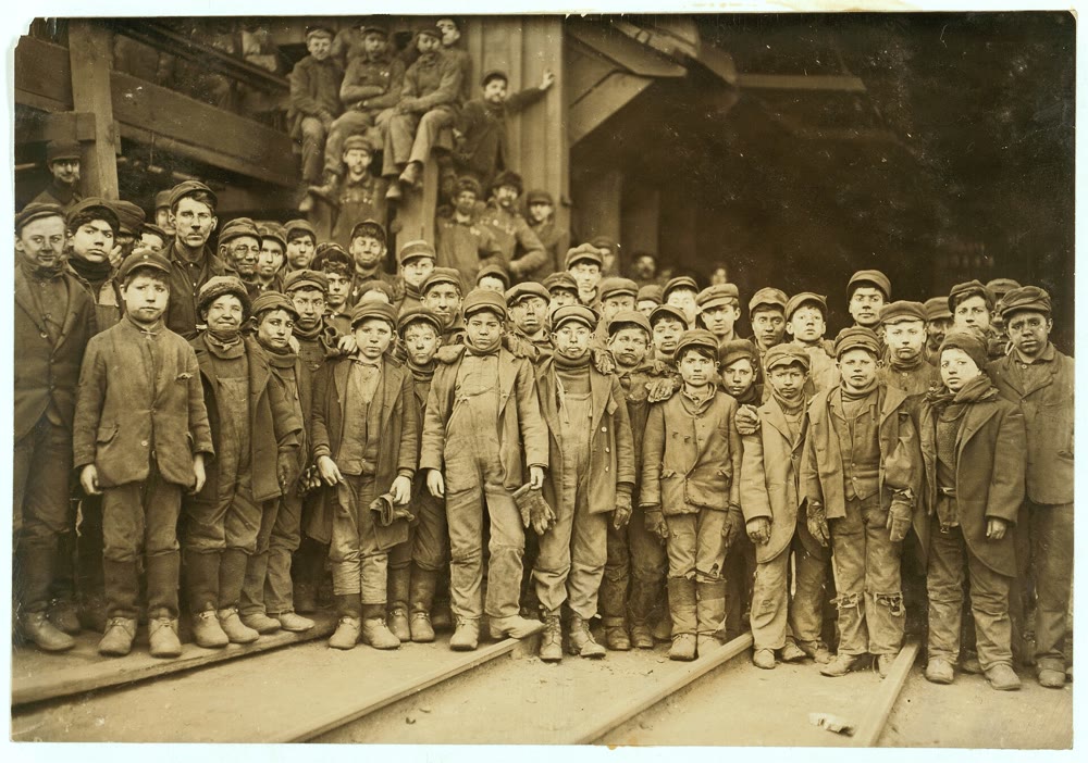 1911 photo of dozens of young breaker boys in caps and coal-dusted clothes standing in rows outside a Pennsylvania coal breaker