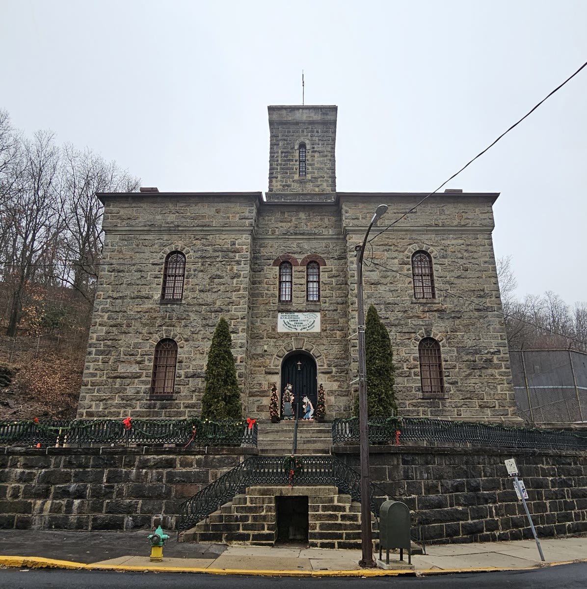 The old Carbon County Jail in Jim Thorpe, Pennsylvania: a grey stone front with a square tower, barred arched windows and steps up to the door