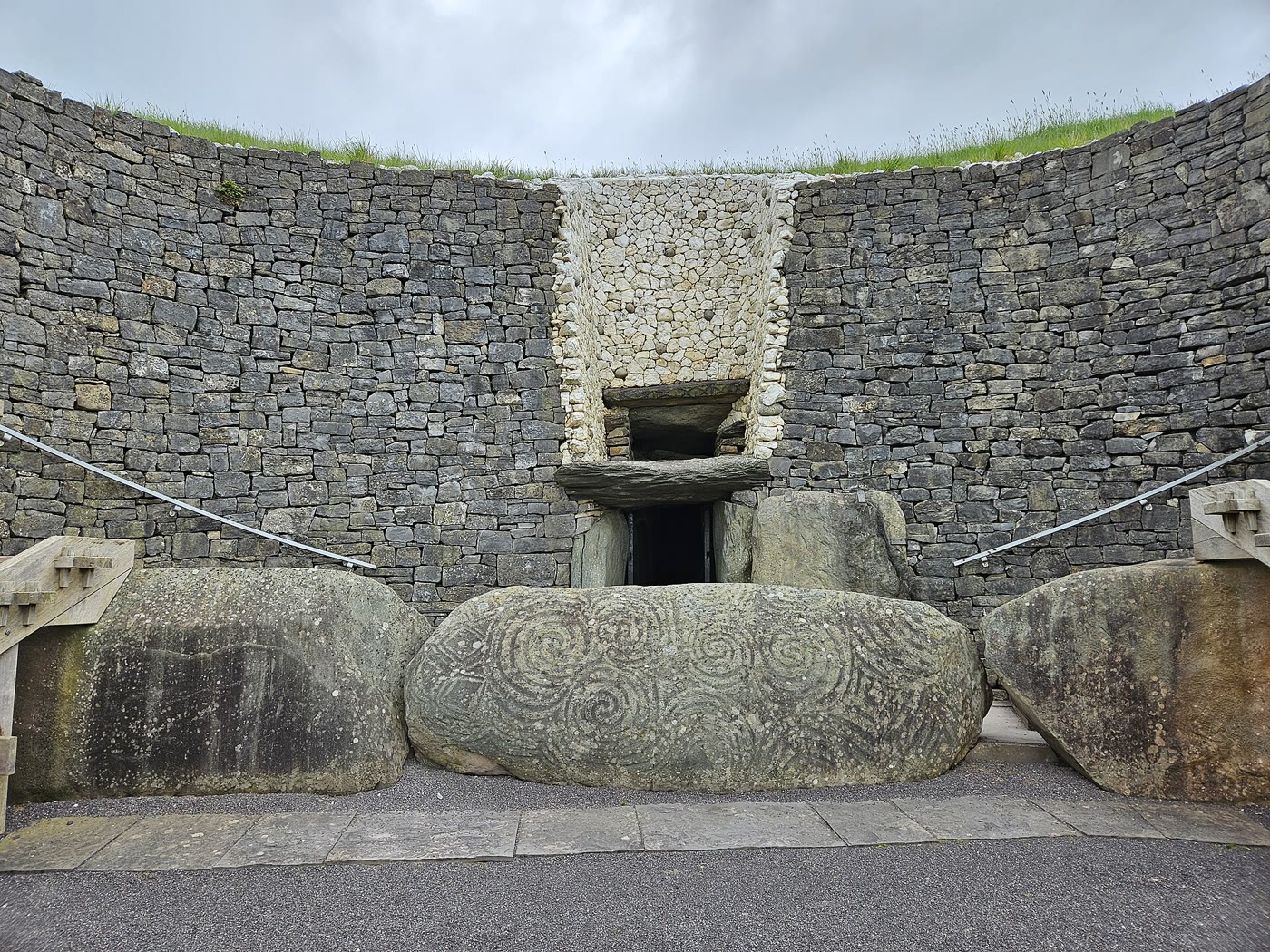 Newgrange entrance stone carved with spirals and lozenges in front of the dark doorway, with the rectangular roof-box opening above it