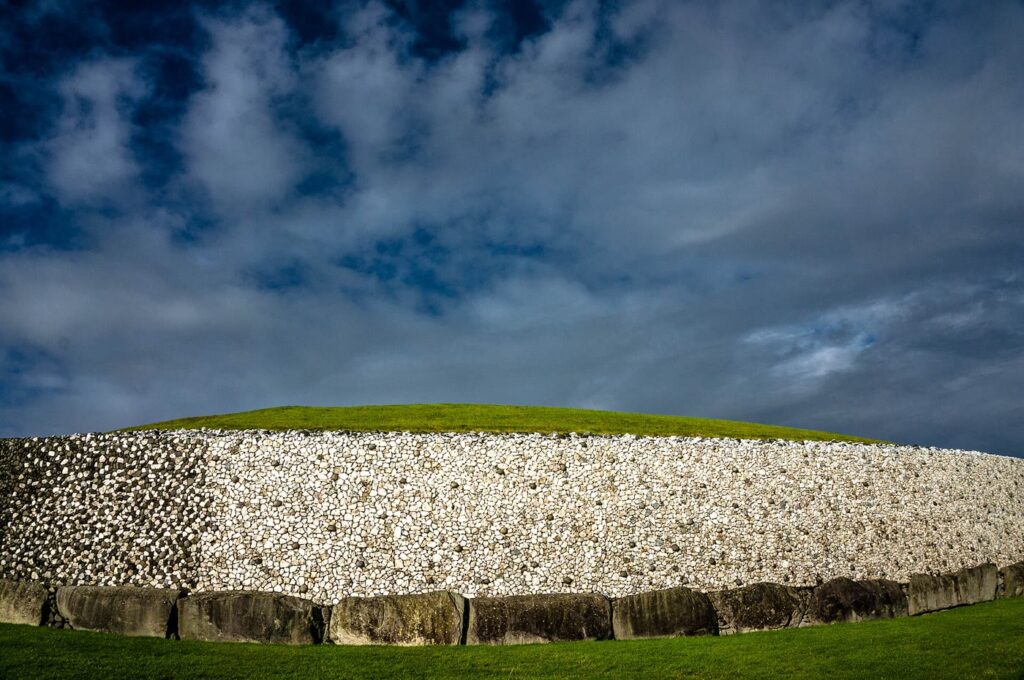 Newgrange passage tomb: the white quartz and granite front wall above a ring of grey kerbstones, under a dark blue cloudy sky