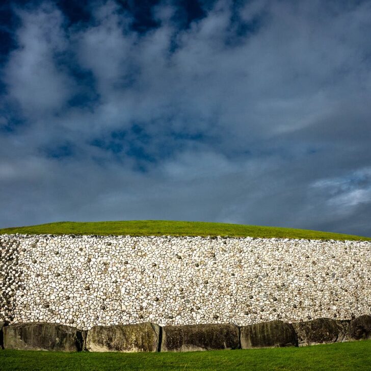 Newgrange passage tomb: the white quartz and granite front wall above a ring of grey kerbstones, under a dark blue cloudy sky
