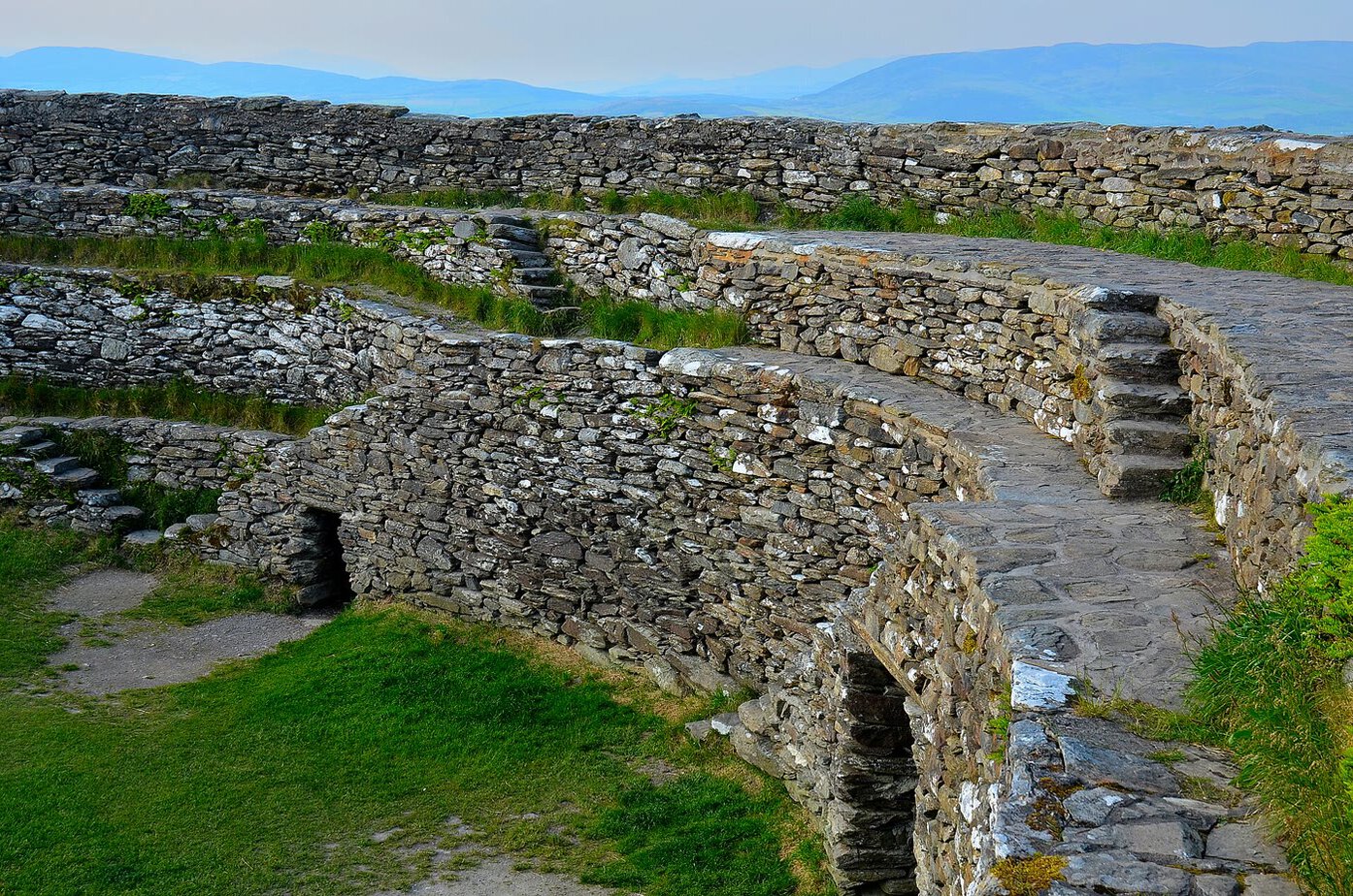 Terraced dry-stone walls and stone steps inside the circular Grian&aacute;n of Aileach fort in Donegal, with hills fading into haze beyond