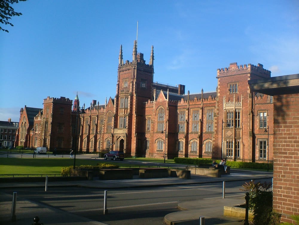 The red-brick Lanyon Building of Queen's University Belfast with its central tower and pinnacles, lawns in front, under a clear blue evening sky