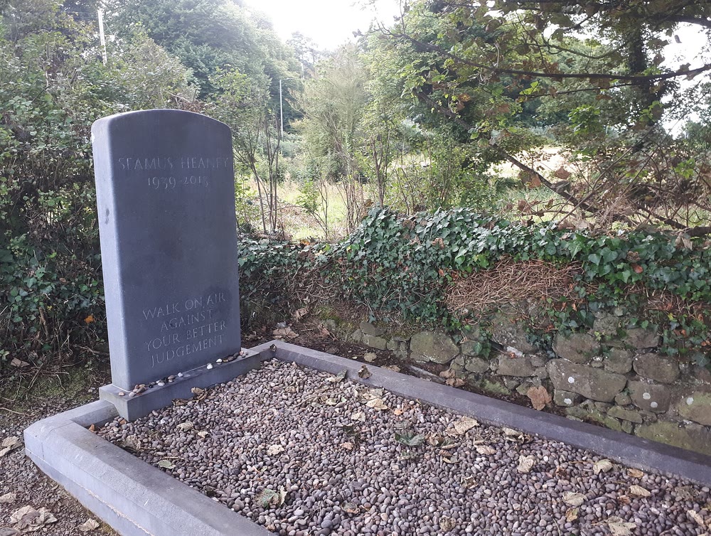 Seamus Heaney's plain grey headstone, inscribed with his name, his dates and his epitaph, above a grave of small pebbles beside an ivy-covered stone wall