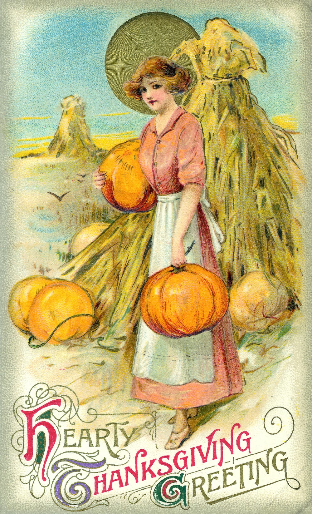 Vintage Thanksgiving postcard of a young woman in a pink blouse and white apron carrying two pumpkins past sheaves of corn, with the words Hearty Thanksgiving Greeting in ornate lettering