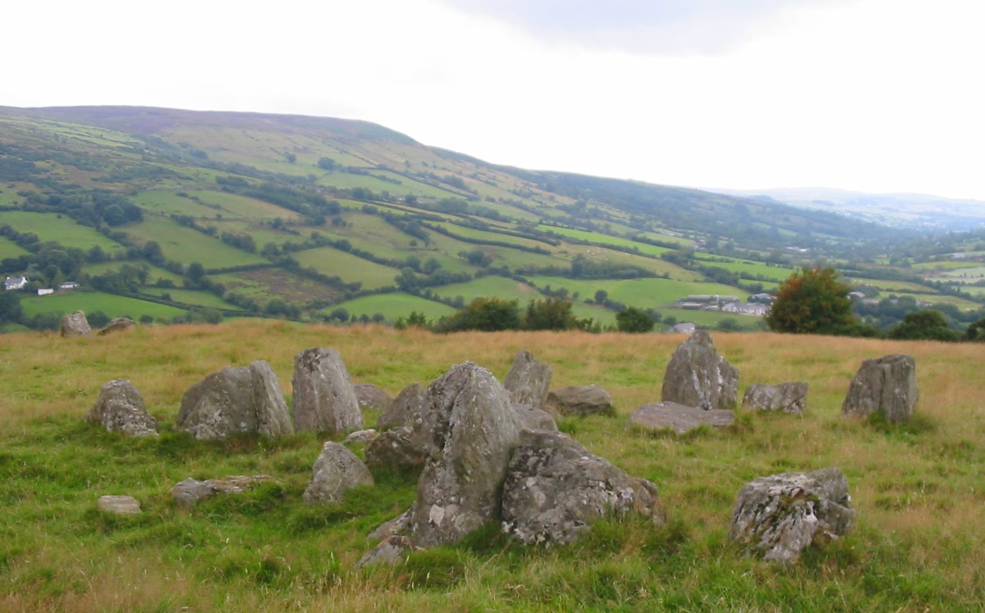Ossian's Grave court tomb: weathered grey standing stones in rough grass on a hillside in Glenaan, Co. Antrim, with green fields and hills behind