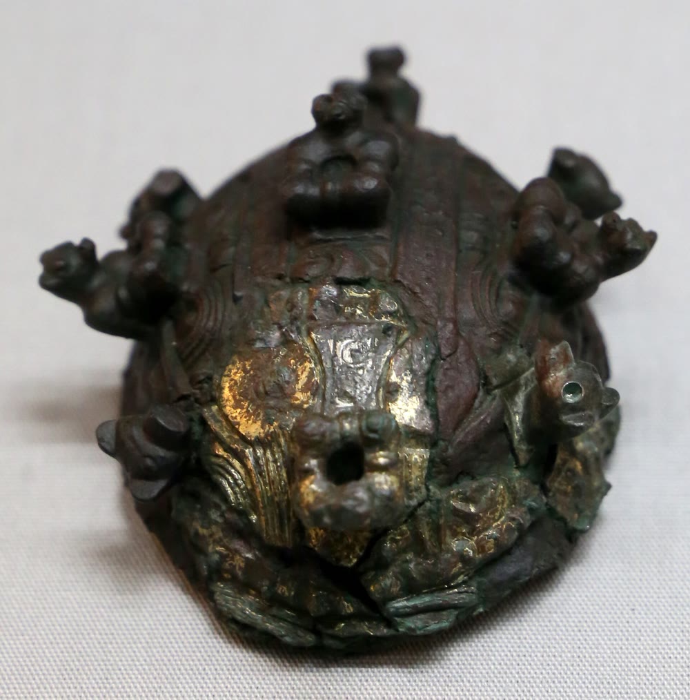 A domed oval Viking brooch of dark bronze with traces of gilding, decorated with small cast animal heads and bosses, photographed against a pale background